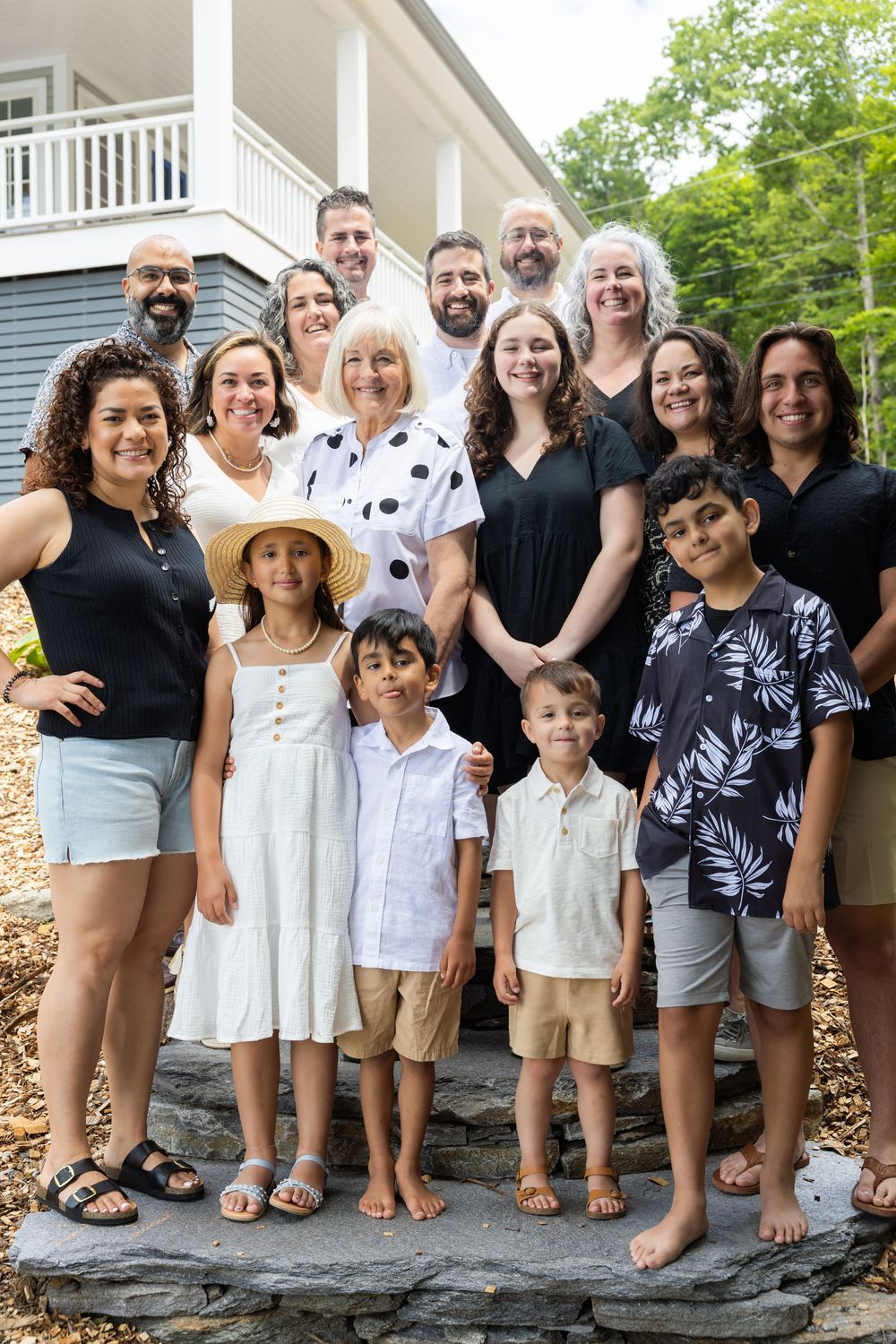 A large family group poses together on stone steps outside a house wearing coordinated black and white summer outfits.