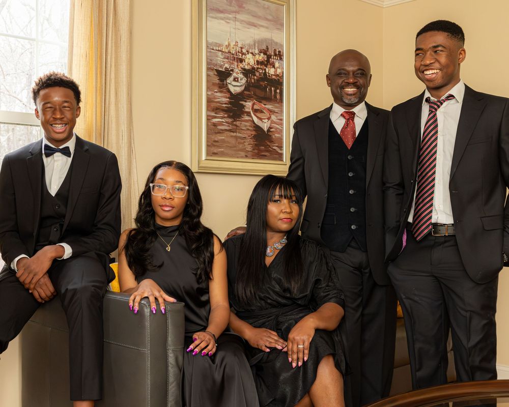 A formal group portrait of five people in elegant black attire posing together in a living room setting.