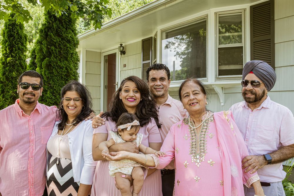 A group wearing coordinated pink and white outfits poses together outdoors in front of greenery.