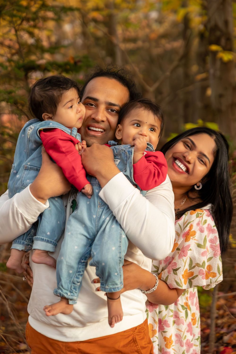 A family shares joyful moments together outdoors during an autumn photoshoot with fallen leaves in the background.