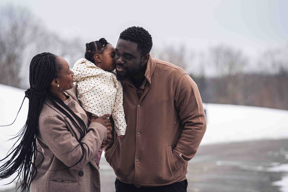 A couple in winter coats shares an intimate moment together in a snowy outdoor setting.