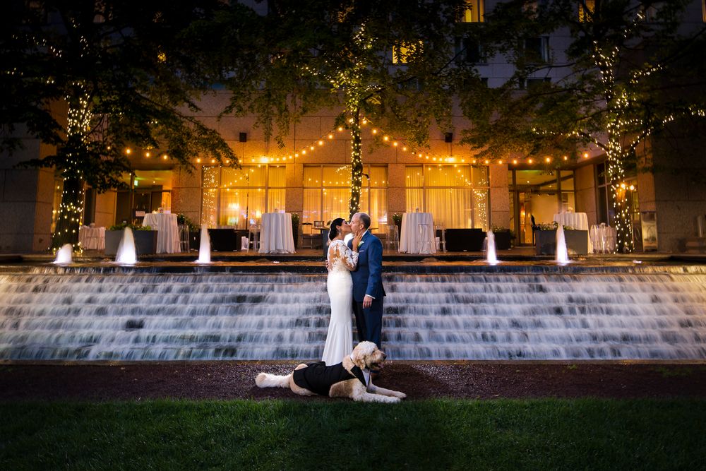 A romantic couple sits on stone steps at dusk with string lights glowing in the trees above them.