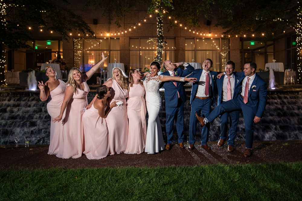 Wedding party poses together under string lights at outdoor evening celebration.