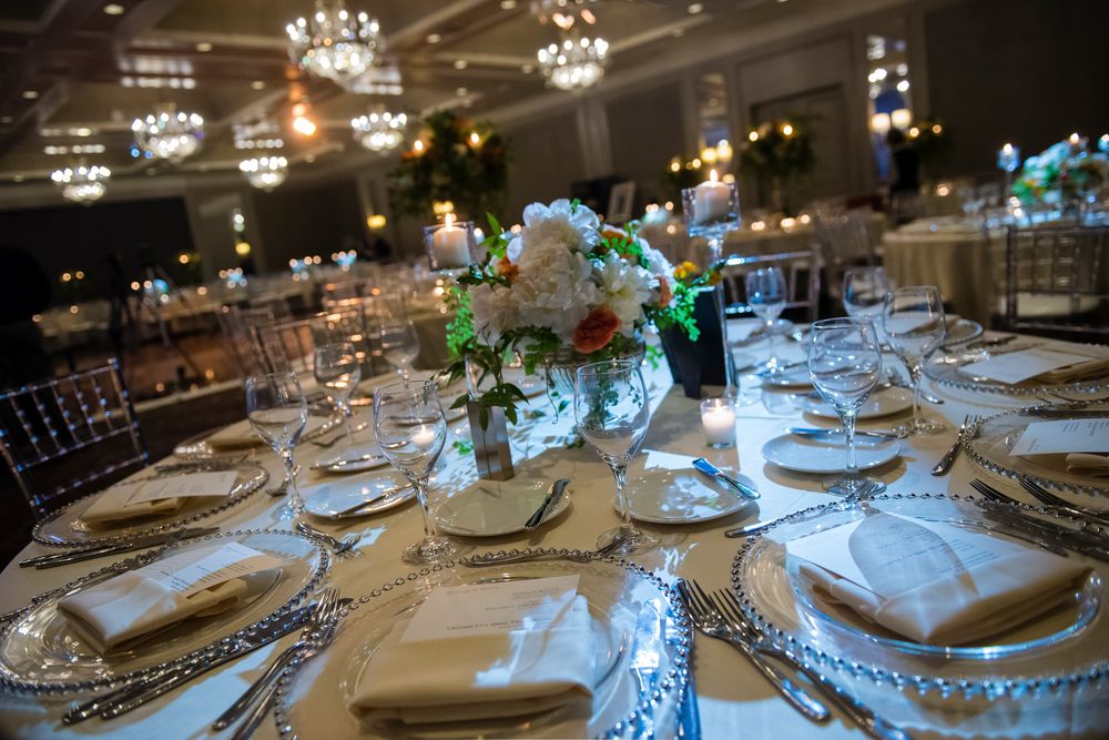 Elegant wedding reception table settings with crystal chandeliers, white linens, and blue floral centerpieces.