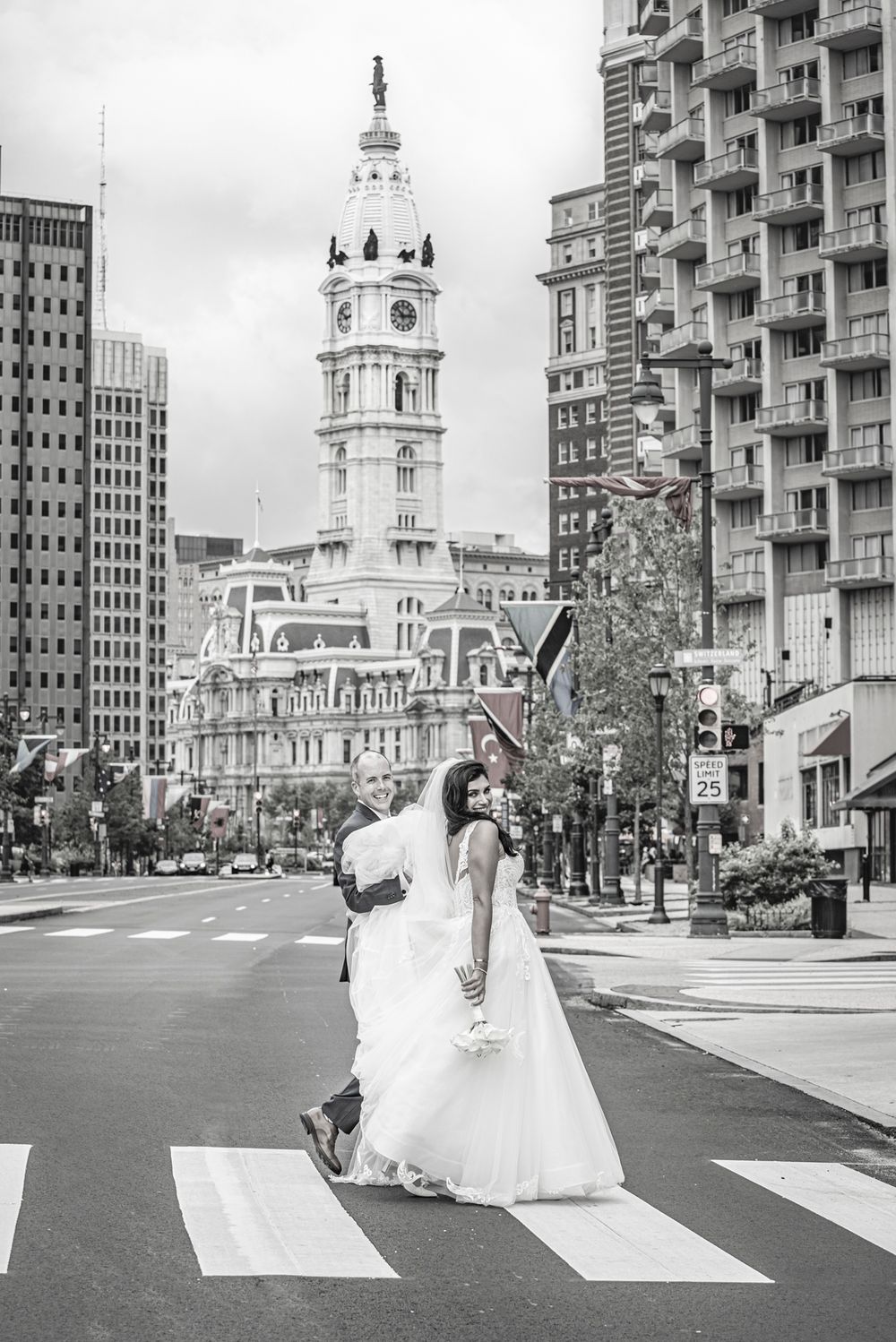 Wedding couple crosses street near Philadelphia City Hall in black and white photography.