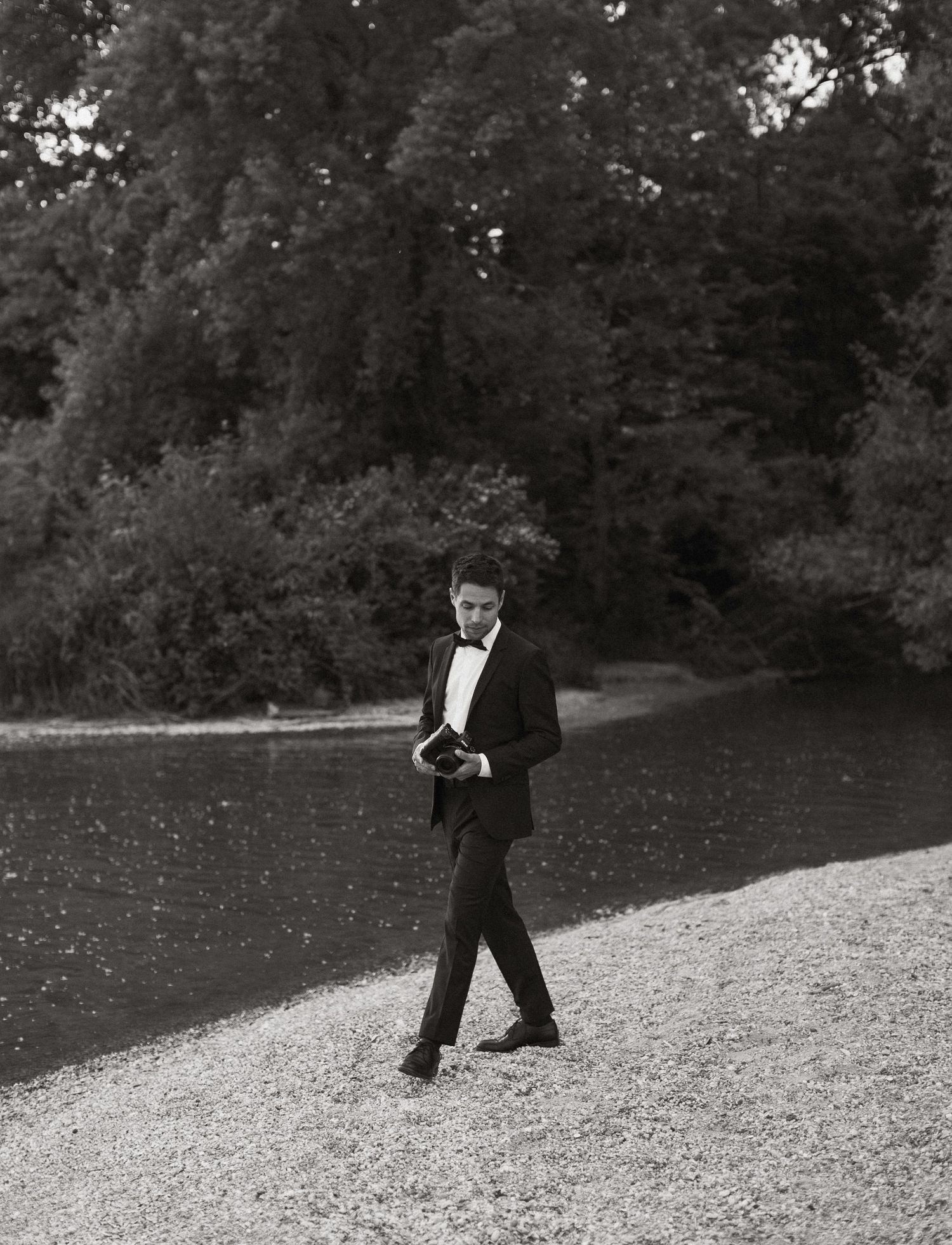 A formal black and white photo of someone walking on a gravel path surrounded by trees.