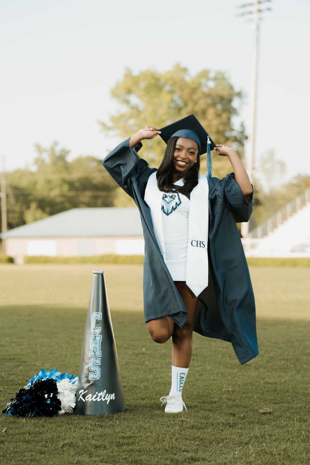 A graduation photoshoot on a grassy field featuring a cap and gown with Nike sneakers and decorative bottles.