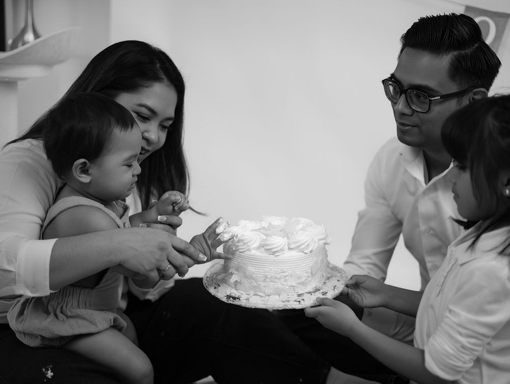 Family gathered around a white birthday cake in a black and white photo celebrating baby's first birthday.
