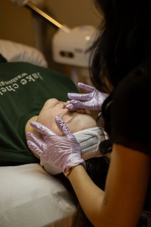 Esthetician wearing purple gloves performing a facial treatment on a client in a spa.