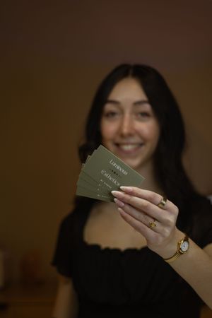 Smiling woman holding fan of green Luminous Esthetics gift cards toward camera with gold watch.