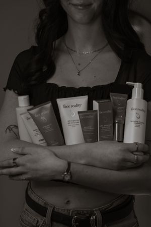 Woman holding multiple Face Reality skincare products in black and white photo.