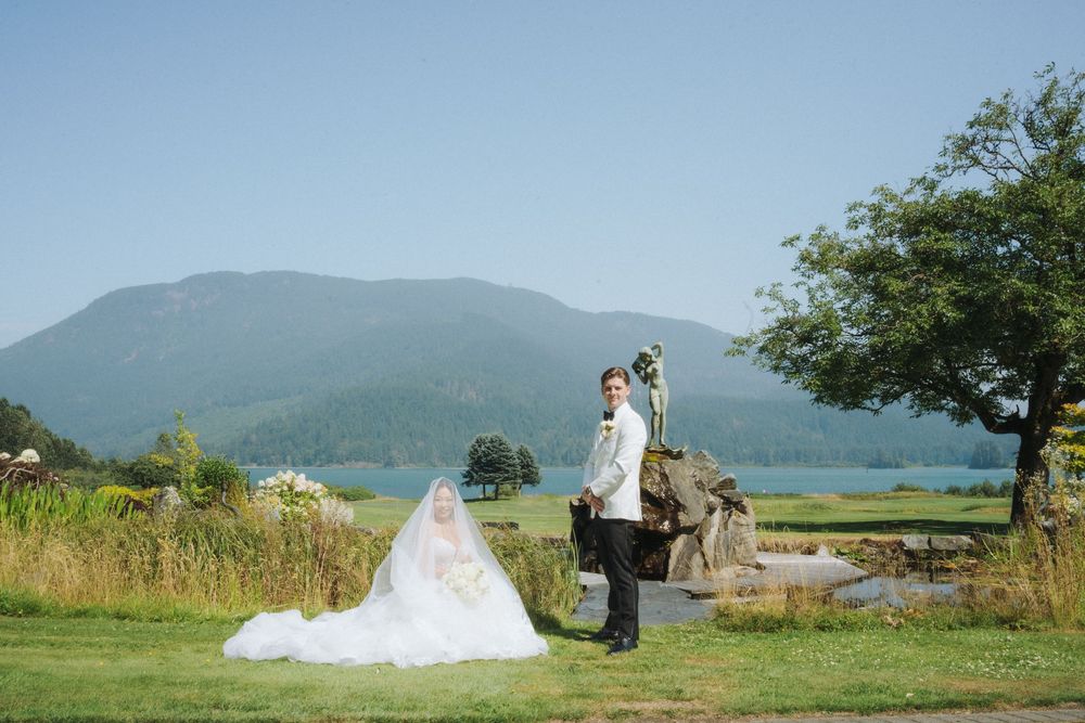 Bride and groom pose in a scenic outdoor wedding portrait with lush mountains and a lake in the background.