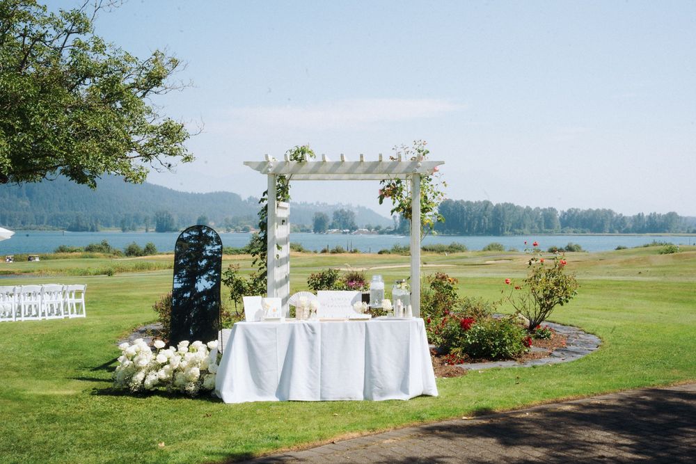 Elegant outdoor wedding ceremony setup with a white arbor, floral arrangements, and a serene lakeside backdrop.