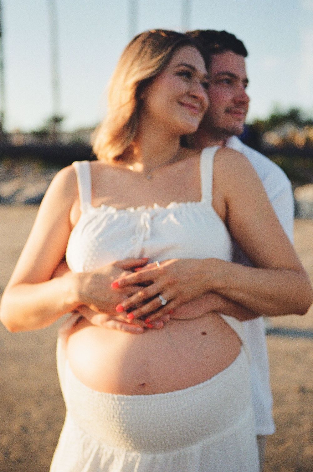 Intimate film maternity photography of a couple embracing in a sun-drenched field in Ventura County, highlighting the timeless film nature