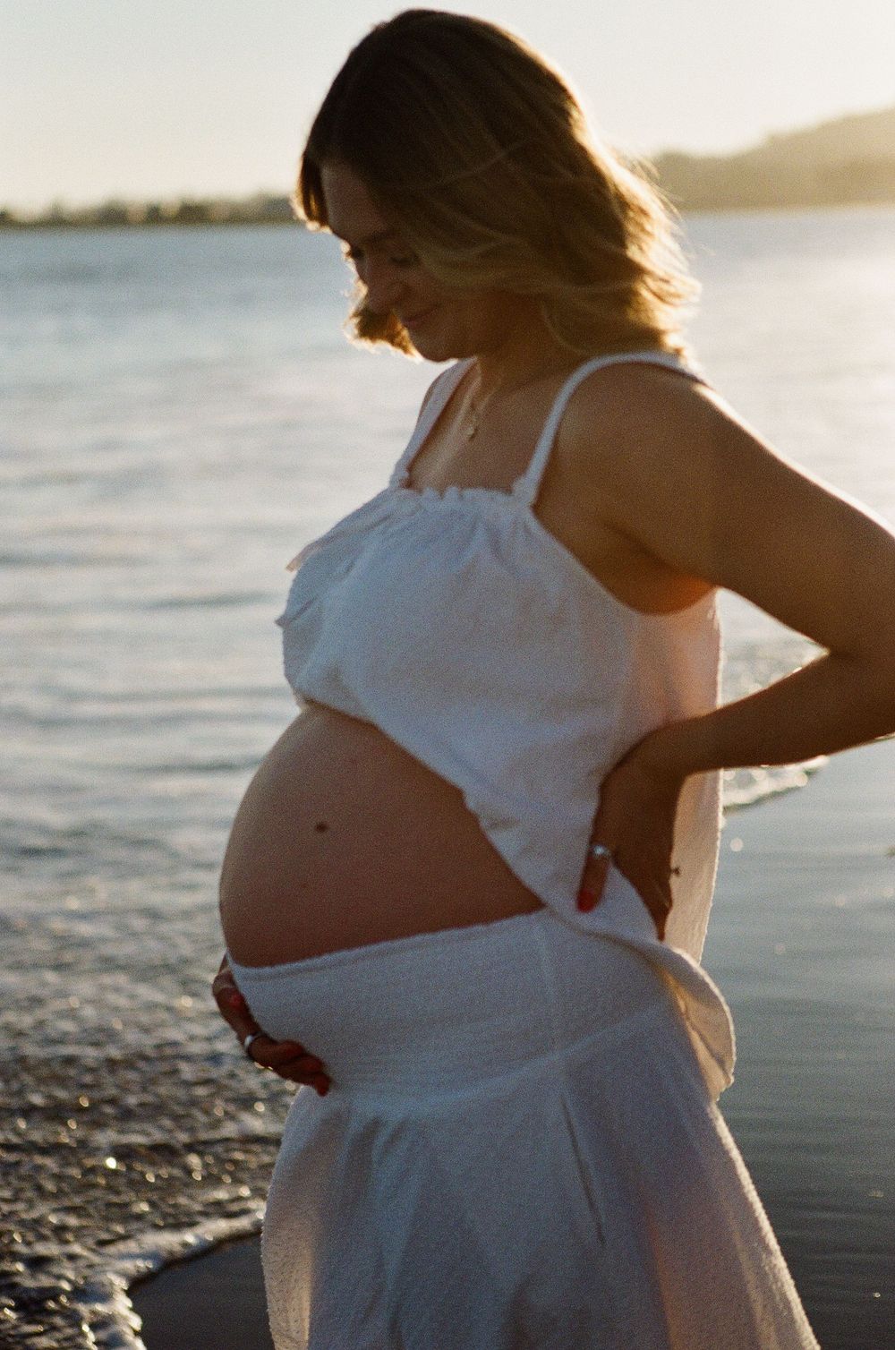 Close-up film portrait of a pregnant woman wearing a soft linen dress, showcasing the organic skin tones and dreamlike quality of film photo