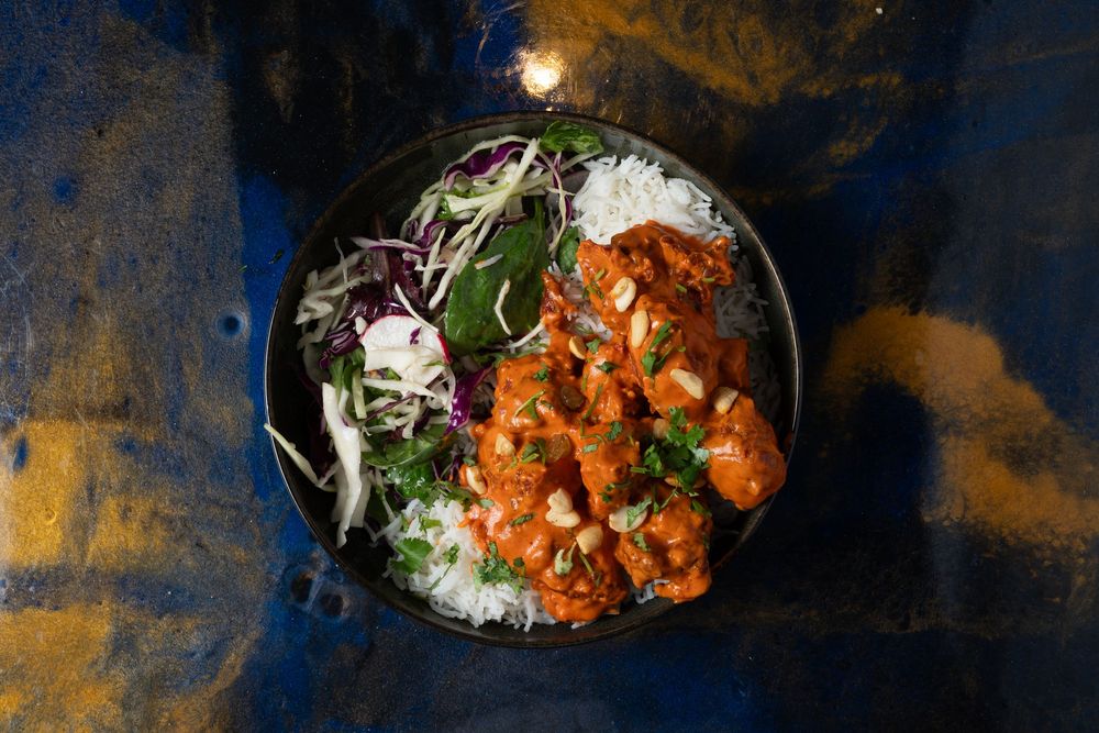 Overhead view of a rice bowl with spicy orange chicken and purple cabbage slaw on a dark rustic background.
