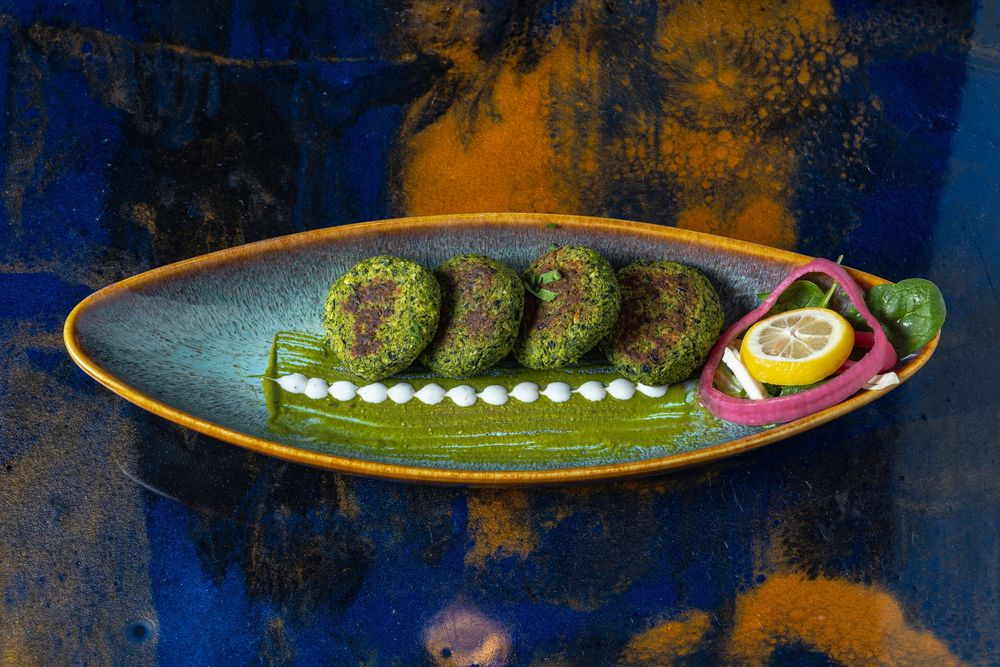 Fresh green peas arranged in a line with cream dots on a dark rustic plate with garnish.