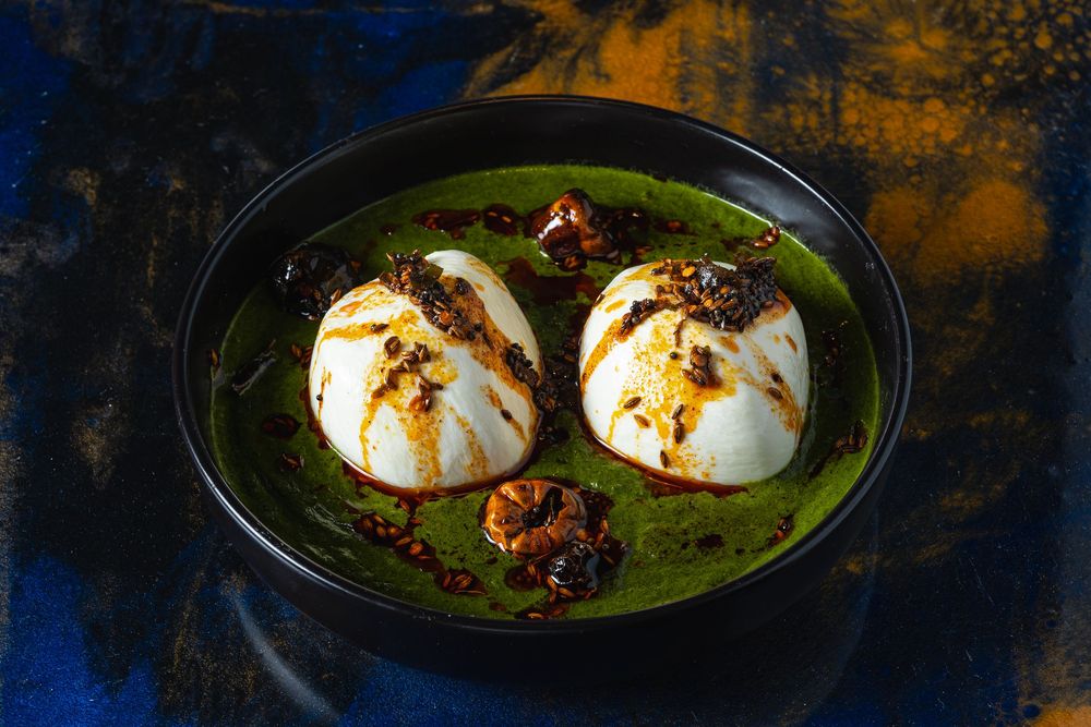 A row of five plated dishes featuring eggs with various garnishes and sauces on dark surfaces.