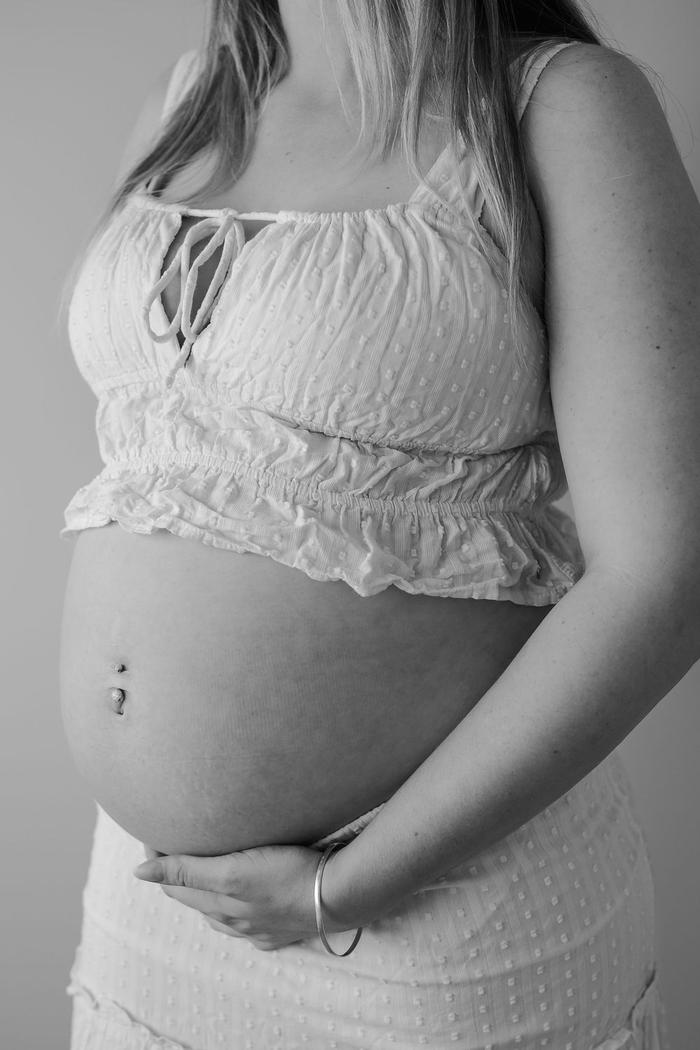 Black and white maternity photo series showing the progression of a pregnant belly in white crop top and bottoms.