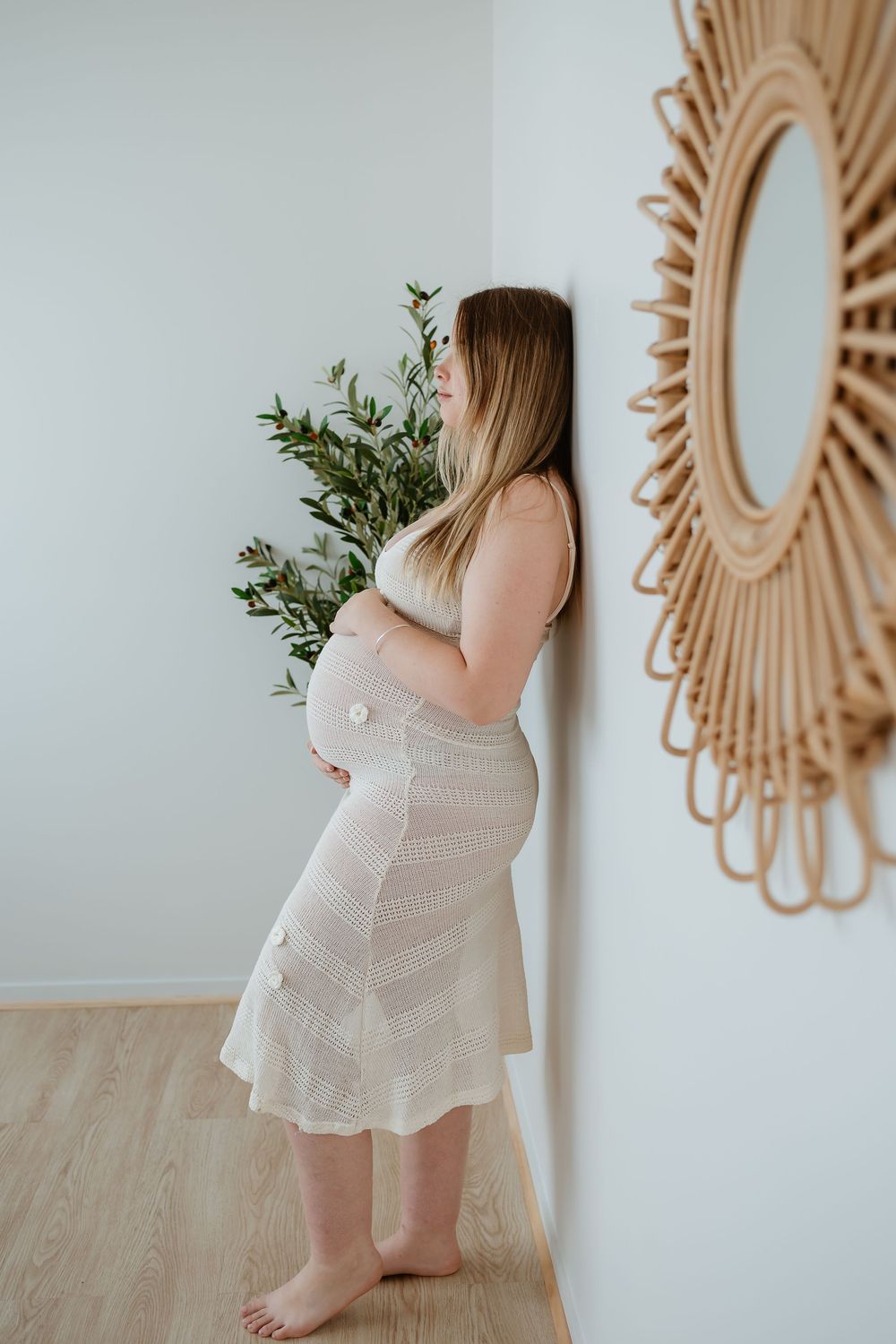 Intimate maternity portrait session with soft lighting and rattan wall decor in a minimalist setting.