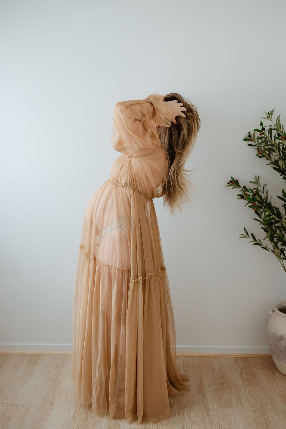 A flowing champagne-colored tulle dress is photographed in sequence against a neutral wall with minimal decor.