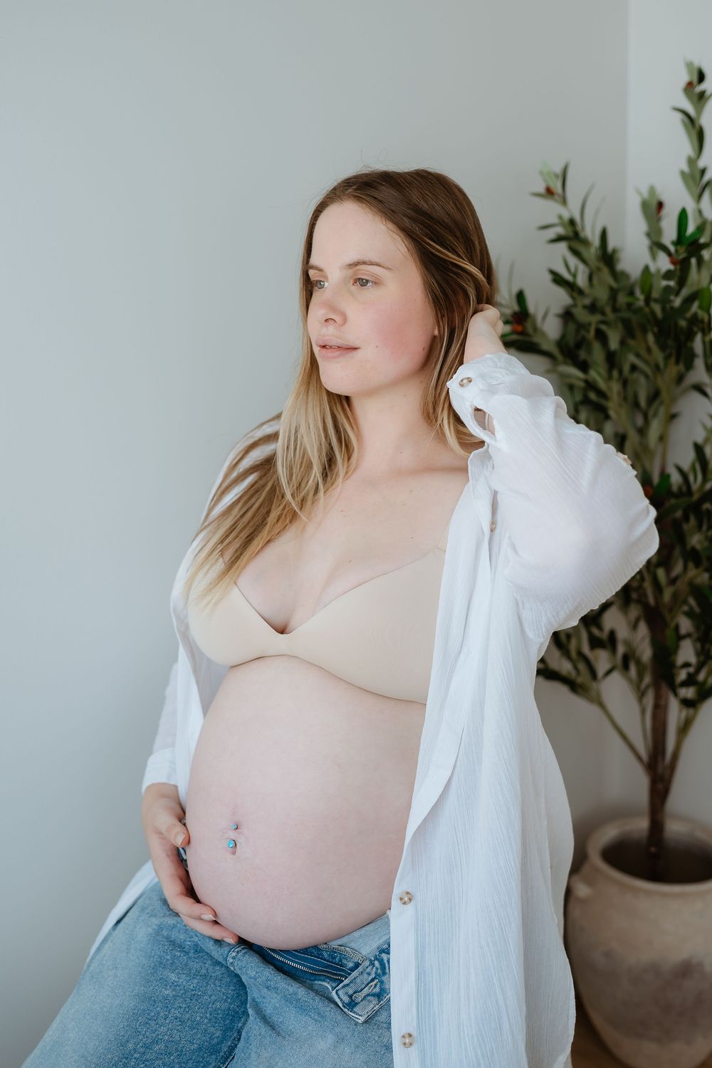 A series of maternity photos showing a pregnant woman in jeans and white top posing against a minimalist backdrop.