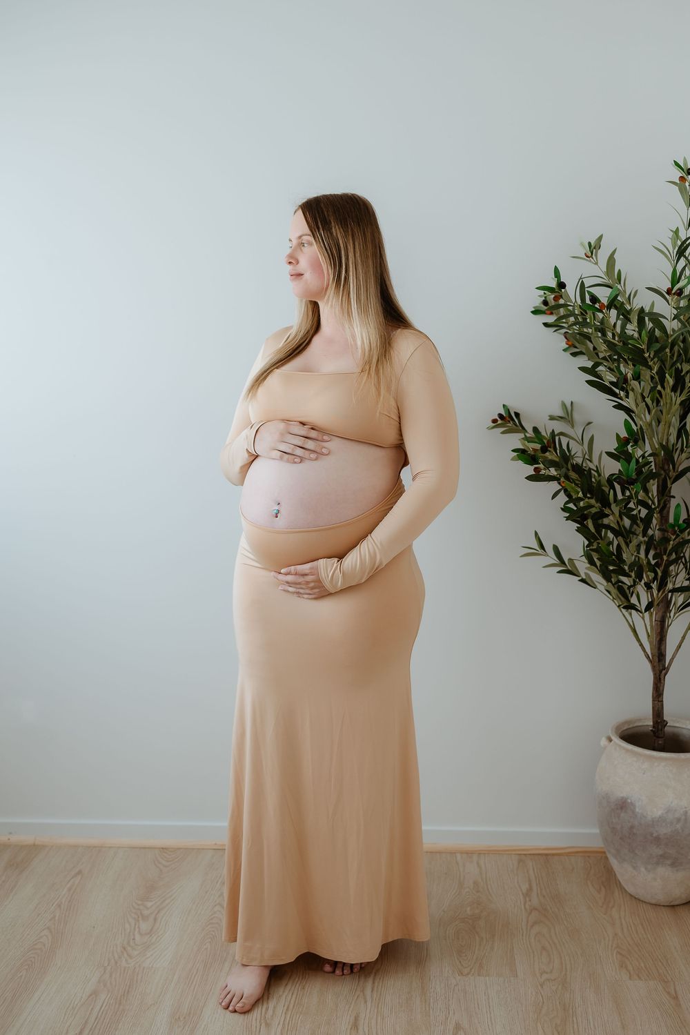 Maternity photoshoot in a light-filled room featuring a peach-colored dress and potted plant decor.