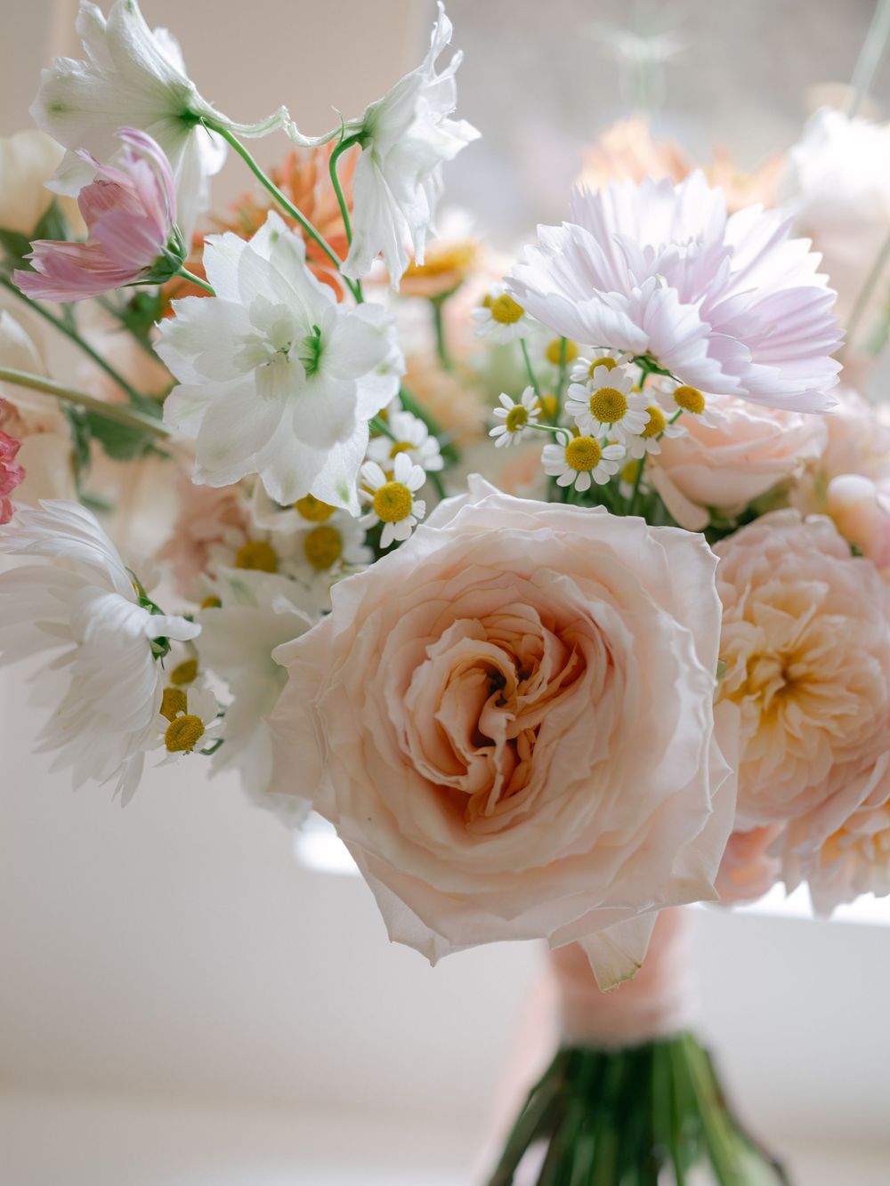 Elegant bridal bouquet featuring blush garden roses, white daisies, and soft pink wildflowers in a romantic pastel arrangement.