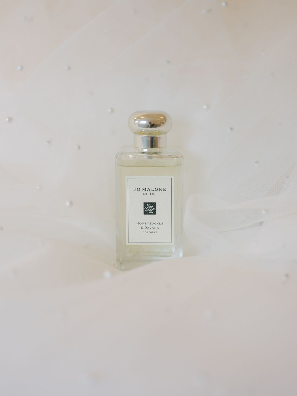 Jo Malone Honeysuckle and Davana cologne bottle on a soft white pearl-embellished background.