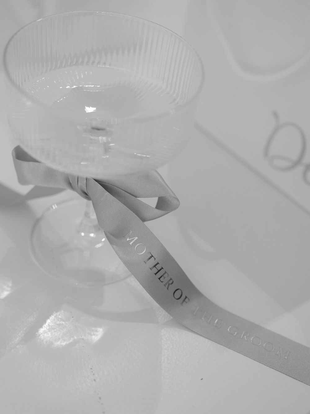 Elegant coupe glass with Mother of the Bride ribbon bow on white tablecloth.