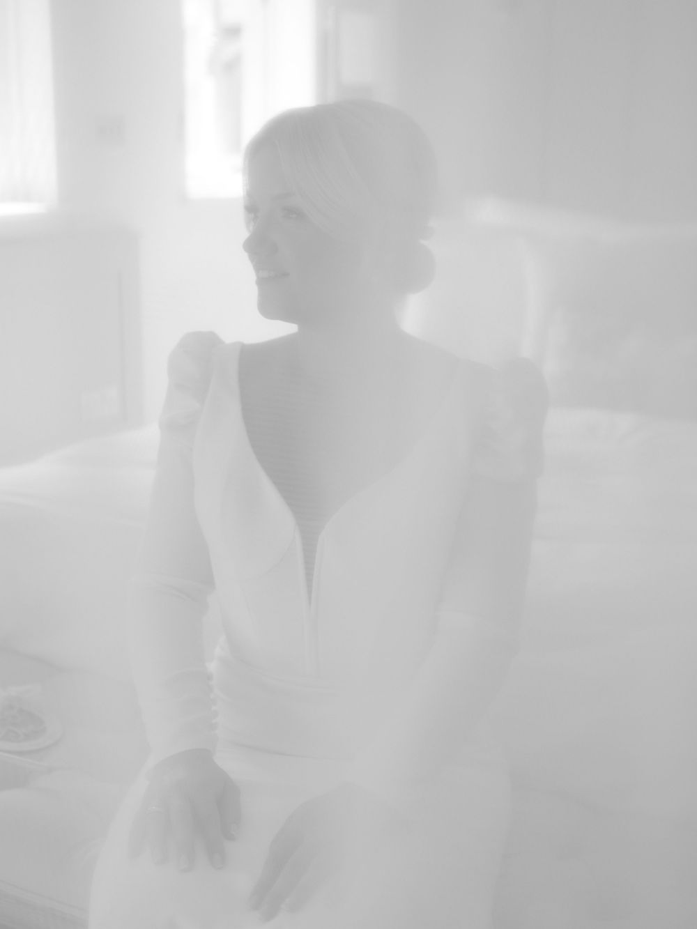 Ethereal soft-focus portrait of a bride in a backless wedding gown smiling in natural light.