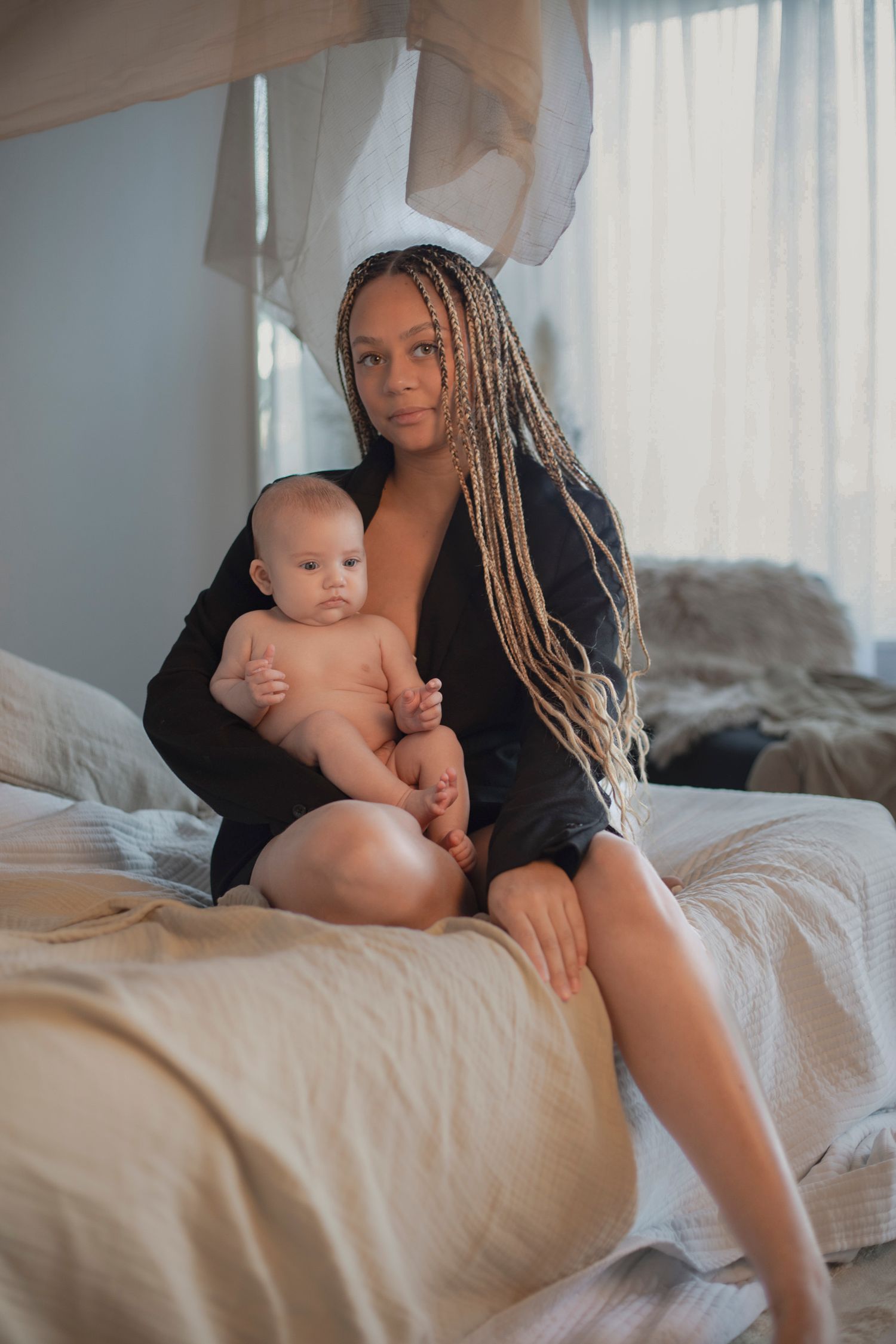 Mamma sitter på sängkanten med sitt barn i famnen. färgerna i bakgrunden är naturfärgade