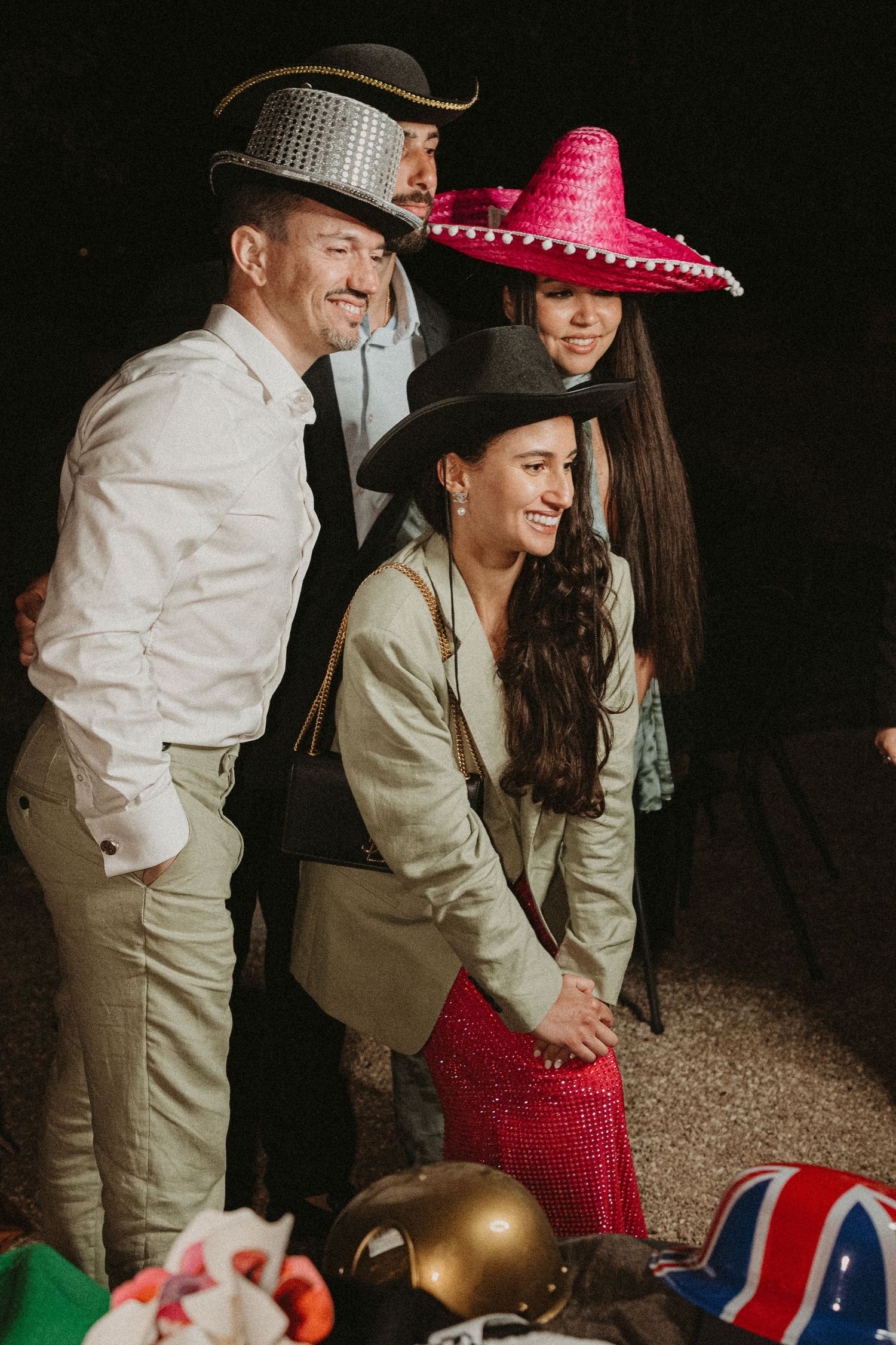 Group wearing western and Mexican style hats pose playfully with props against dark background.