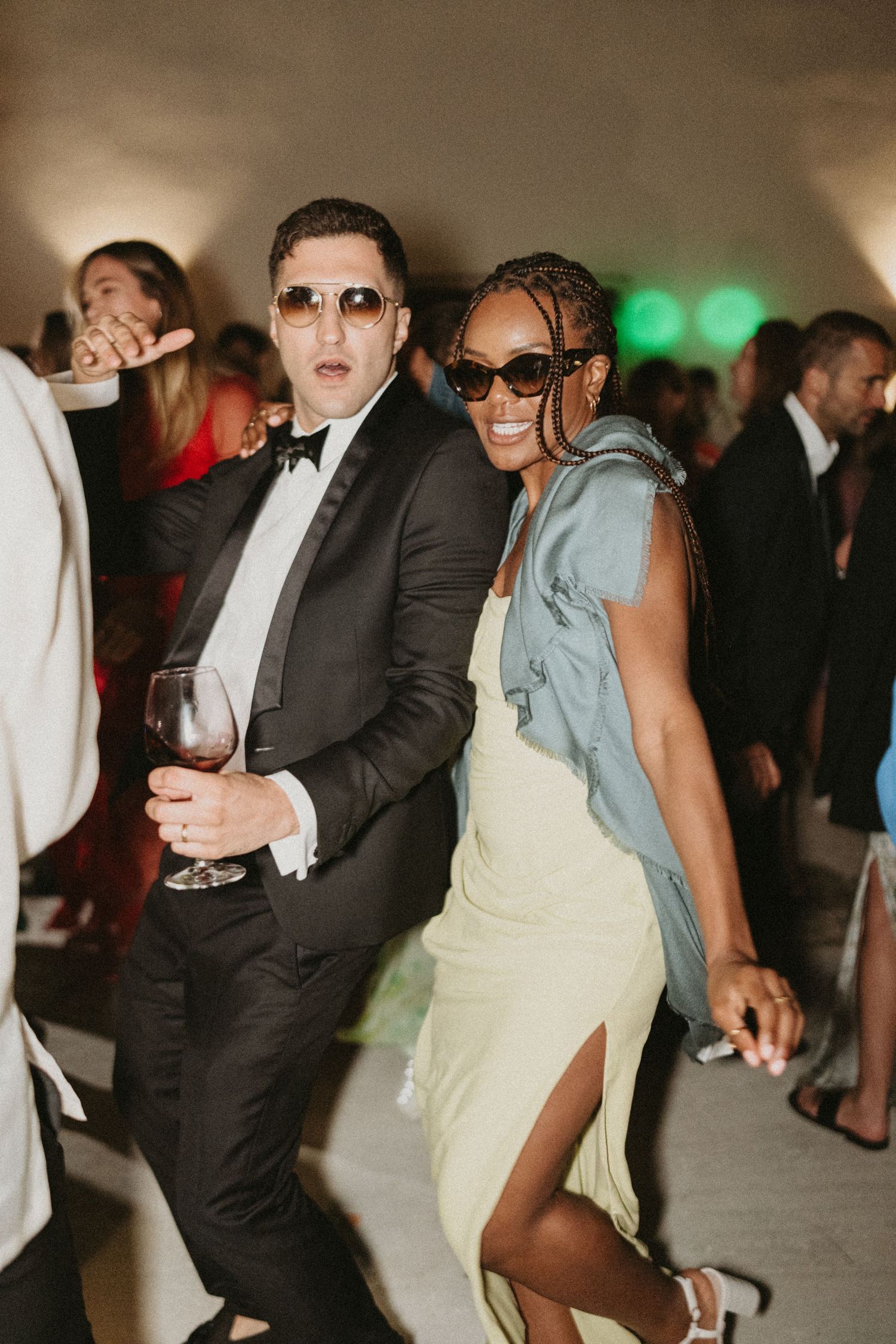 Wedding guests dancing energetically at a reception with people in formal attire under dim lighting.