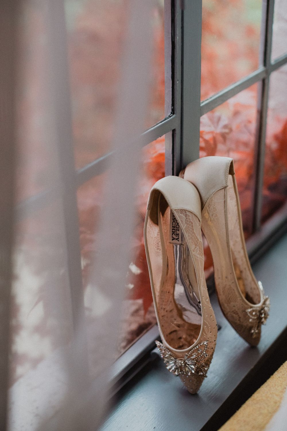 Elegant beige wedding shoes with crystal embellishments displayed on a windowsill with soft bokeh background.