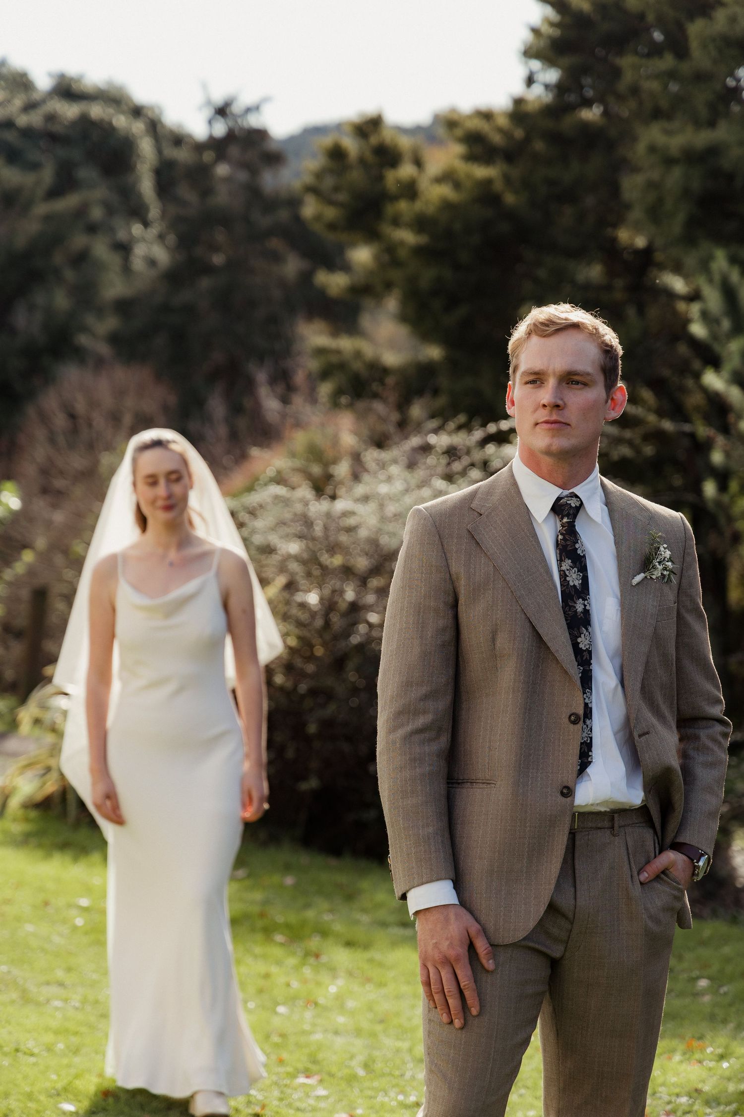 Wedding couple standing in a grassy field with trees in the background. Auckland Wedding Photographer and videographer