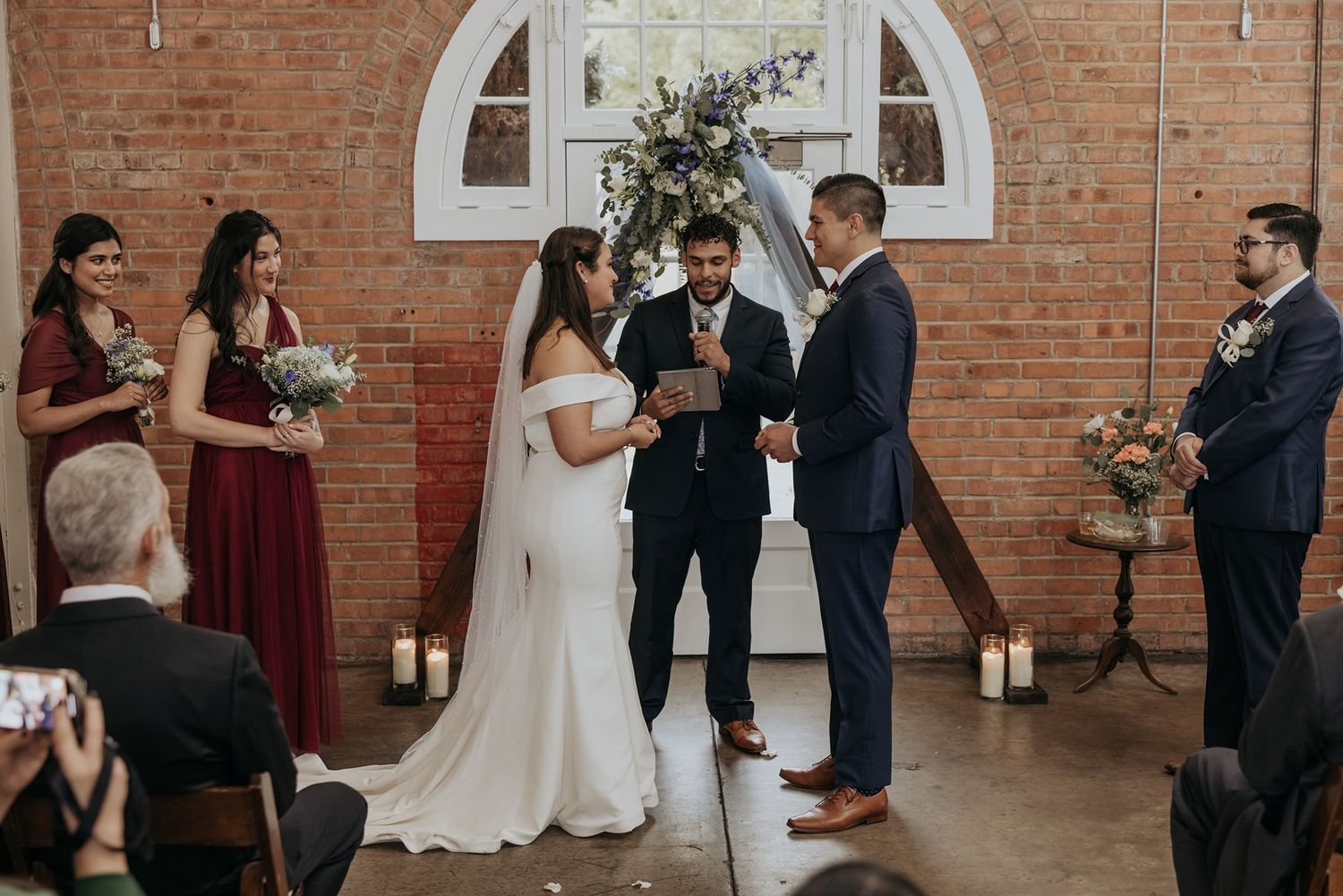 Wedding ceremony in a rustic brick venue with elegant arched windows and romantic lighting.