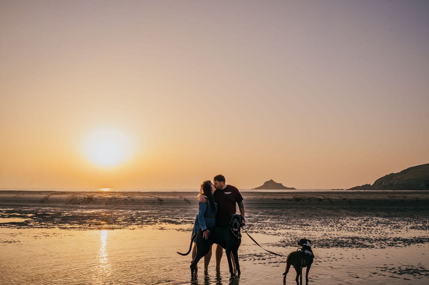 Couple standing on a stone cliff edge overlooking a stunning turquoise ocean under a bright blue sky. Cornwall wedding photographer