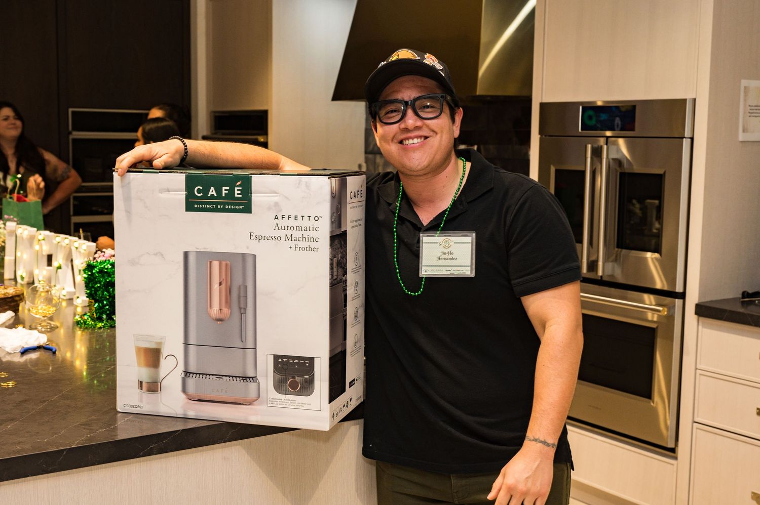 Smiling man in black polo holding a Cafe brand coffee maker box in a kitchen appliance store.
