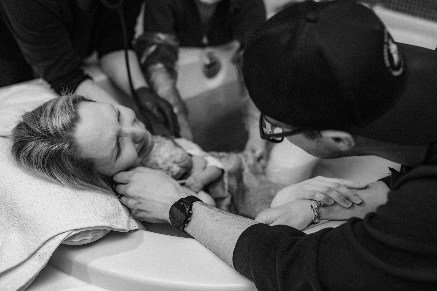 A black and white intimate moment captured between a couple lying down, with one wearing a baseball cap.
