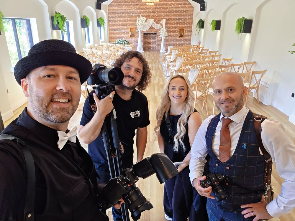 Four wedding photographers and videographers posing inside an elegant white chapel venue with rows of chairs.