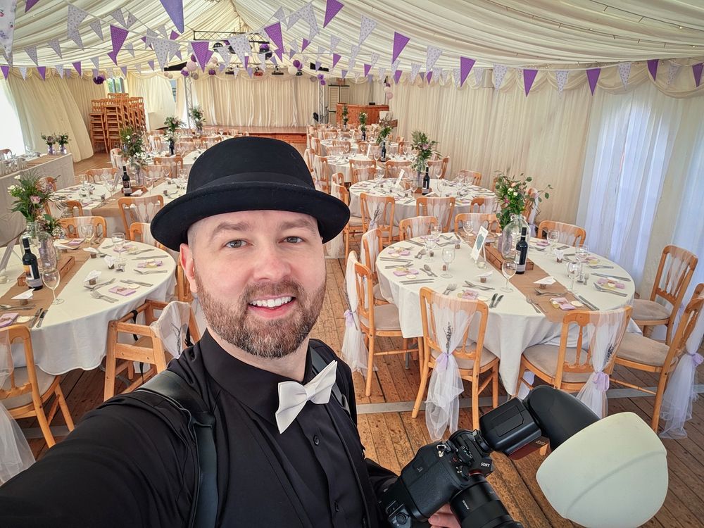 Professional photographer with camera captures selfie in elegant wedding reception marquee with purple bunting.