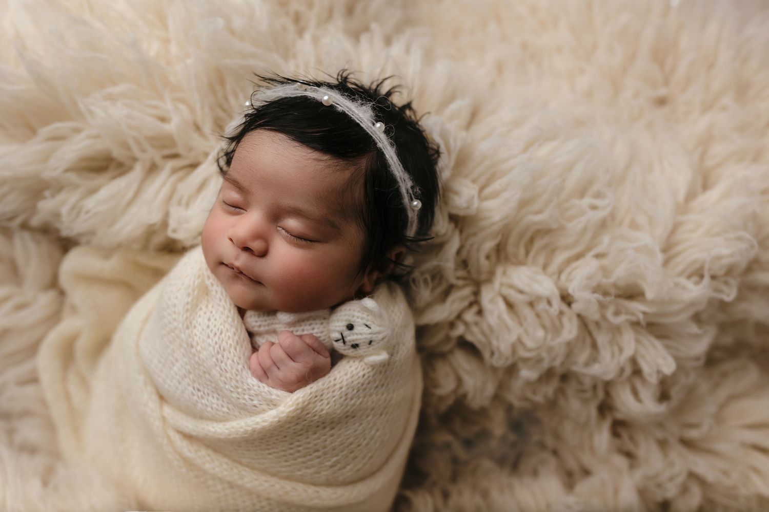 Baby girl sleeps against a neutral fur rug, wrapped and holding a tiny teddy, captured by Charlottesville family and newborn photographer.