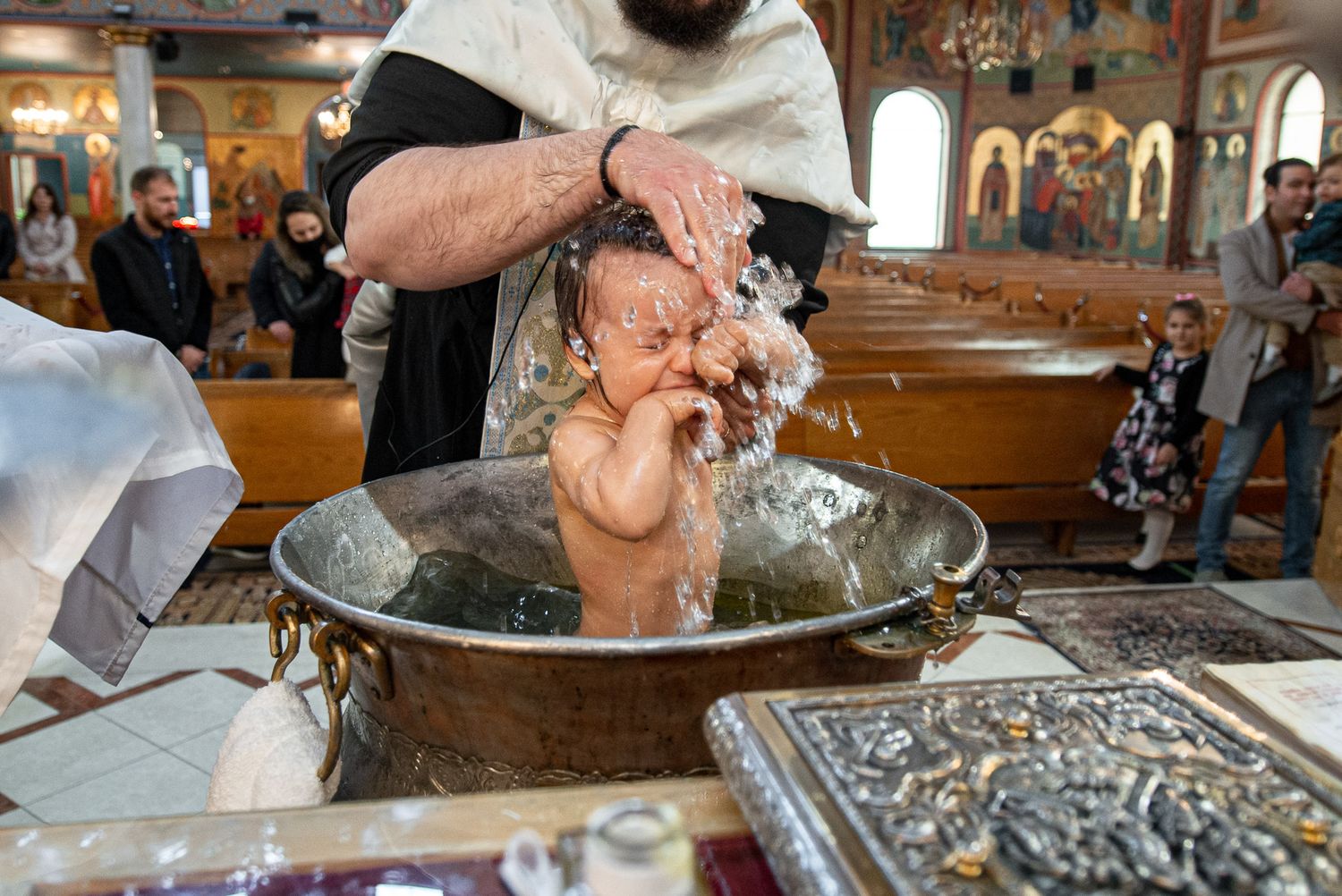 Newborn baby being baptized in ornate golden basin during Orthodox church christening.