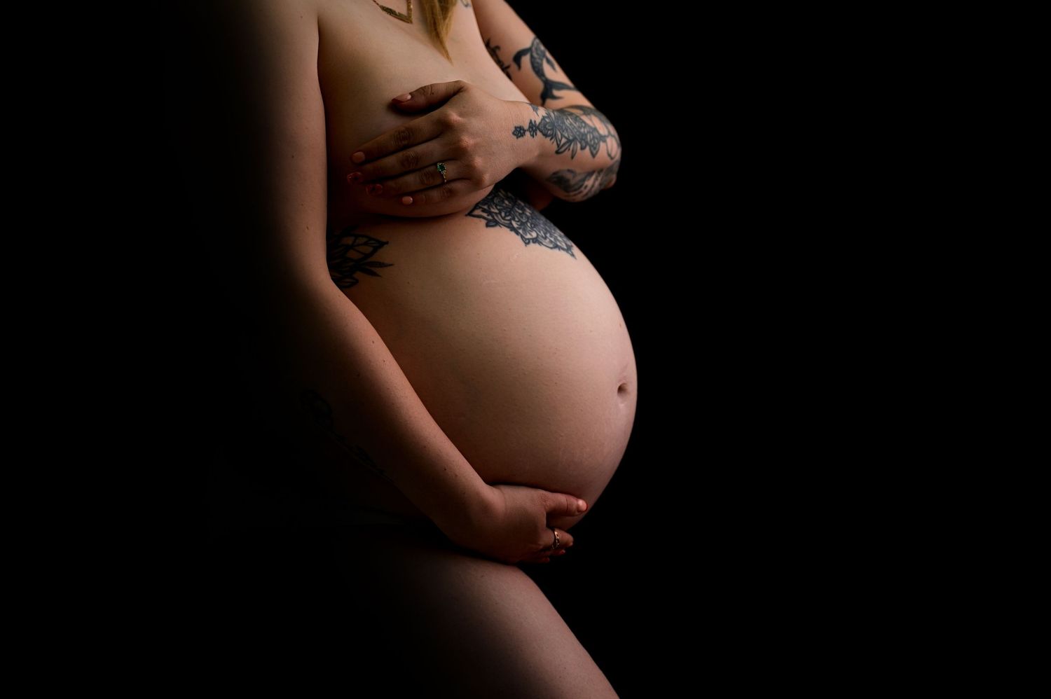 Pregnant woman in flowing white fabric poses gracefully against white background, cradling her baby bump.