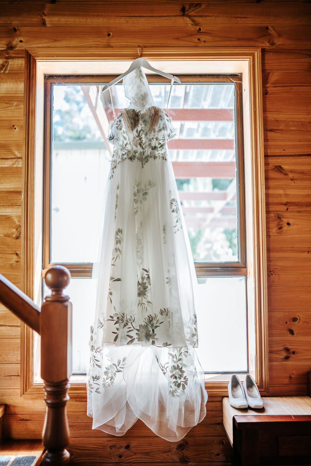 Detail photo of a wedding gown hanging by a big window in a rustic wooden cabin taken by a Melbourne wedding photographer.