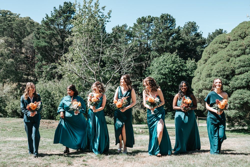 Bridesmaids in green dresses holding bouquets and walking on a straight line laughing taken by a Melbourne wedding photographer.