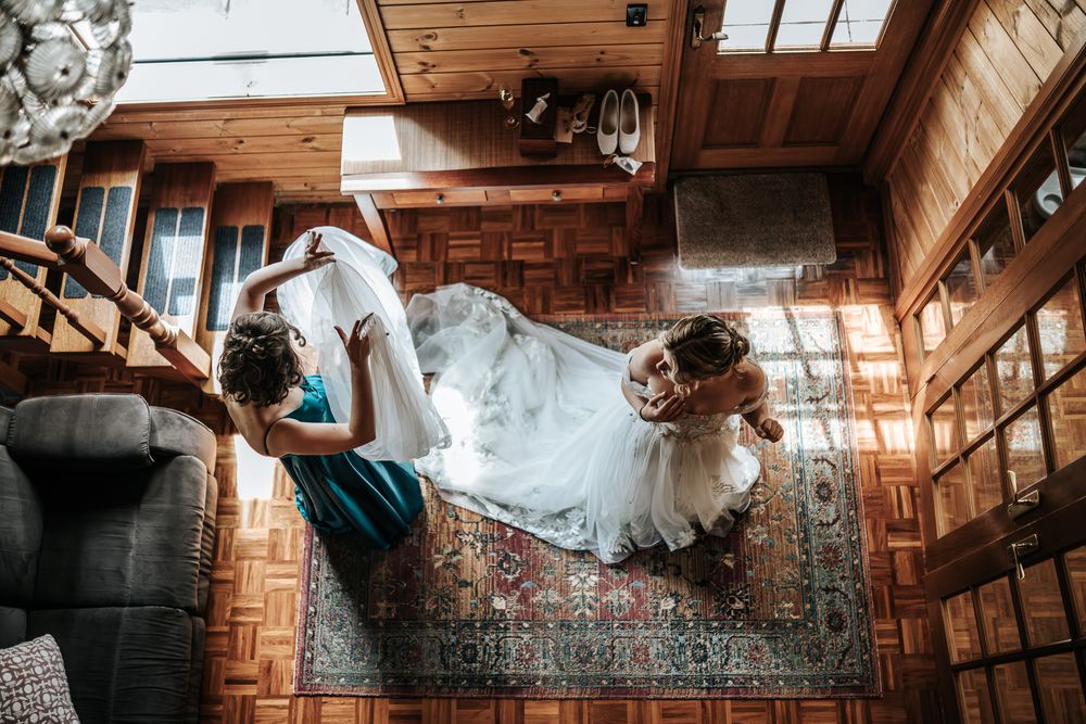 Maid of honor giving a helping hand to the bride while getting ready in wooden cabin taken from the top by a Melbourne wedding photographer.
