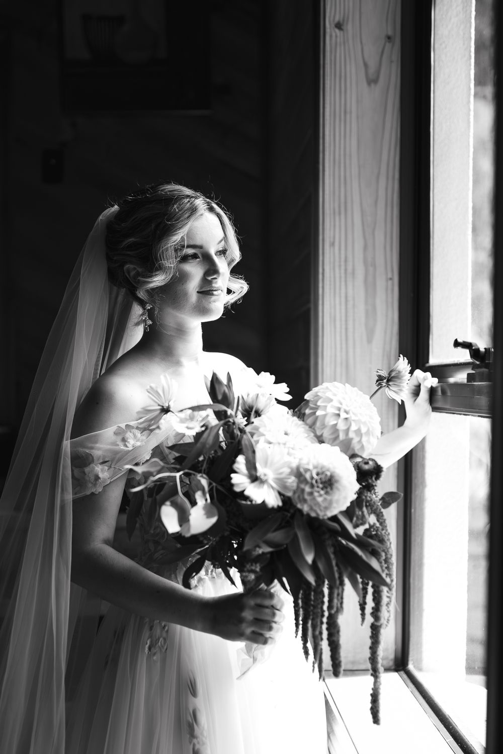 A black and white portrait of the bride with her bouquet in her dress looking outside the windows by Melbourne wedding photographer.