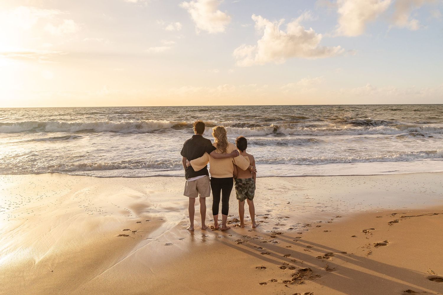 A group of people watching a sunset on a sandy beach with gentle waves rolling onto the shore.